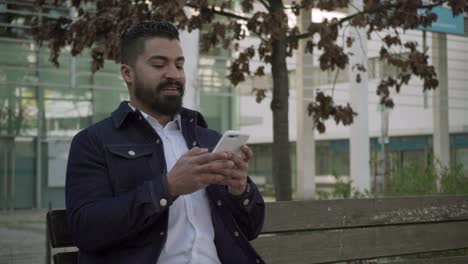 Focused-bearded-man-messaging-via-smartphone-on-street